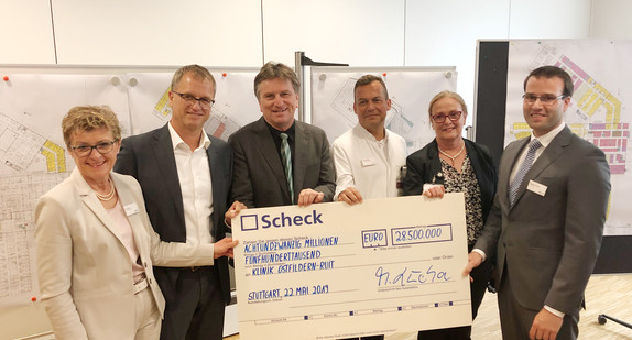 Minister Manne Lucha und Vertreter der medius Klinik Ostfildern-Ruit halten gemeinsam symbolischen Scheck über rund 28,5 Millionen Euro