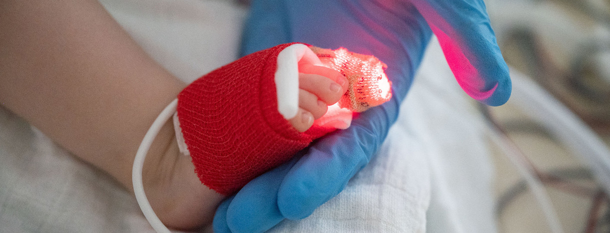 Eine Intensivpflegerin hält den Fuß eines jungen Patienten, der beatmet wird, in der Hand.