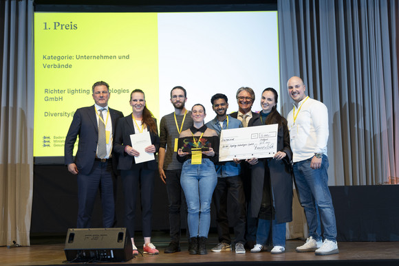 Preisverleihung Integrationspreis des Landes Baden-Württemberg Gruppenfoto der Preisträger von Platz 1 der Kategorie „Unternehmen und Verbände“ mit Minister Manne Lucha auf Bühne.
