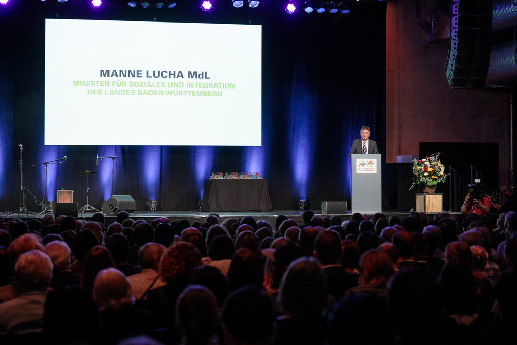 Sozial- und Integrationsminister Manne Lucha spricht vor Publikum in großem Veranstaltungssaal