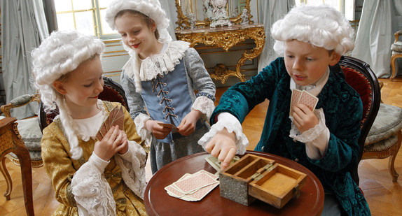 Kinder in Barock-Kostümen spielen Karten