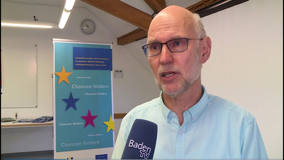 Mann steht neben einer Stellwand mit ESF-Poster und spricht in Baden-TV-Mikrofon