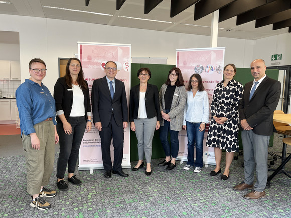 Gruppenfoto: Staatssekretärin Dr. Ute Leidig steht mit mehreren Mitgliedern des Interkulturellen ÄrztInnen-Netzwerks vor zwei Roll-ups des Netzwerks.