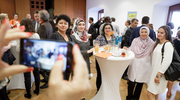 Pressefotos Zertifikatsfeier Qualifizierungsprogramm MEMO Besucherinnen und Besucher an Stehtisch lassen sich fotografieren