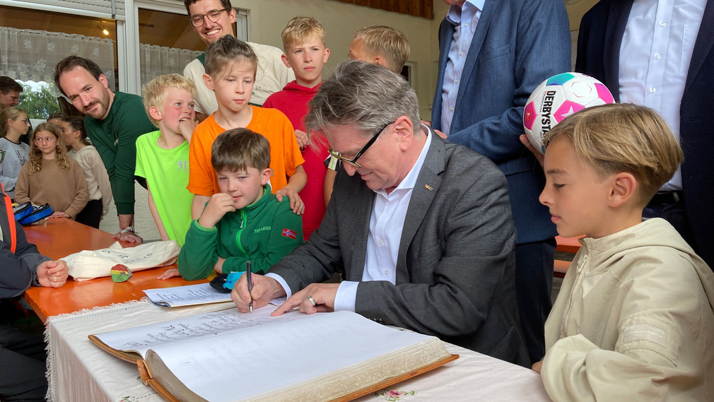 Minister Lucha trägt sich im Beisein von Kindern, Jugendlichen und Betreuern ins Gästebuch des Zeltlagers Zimmerbergsmühle ein.