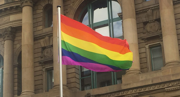 Flagge mit Regenbogenfarben weht vor Gebäude