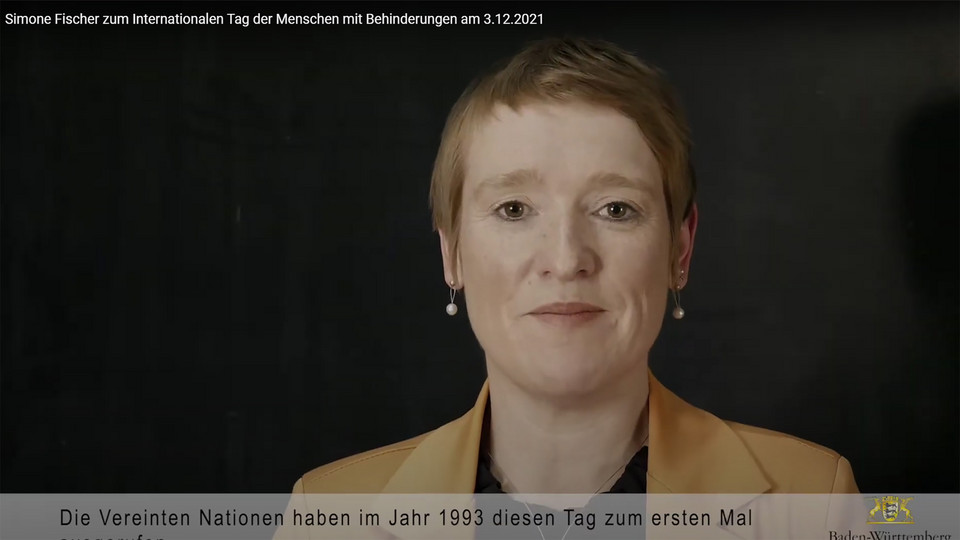 Landes-Behindertenbeauftragte Simone Fischer blickt vor dunklem Hintergrund in die Kamera.