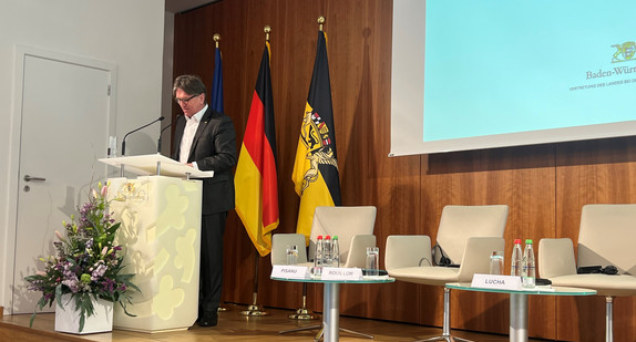 Minister Manne Lucha an Redepult vor großer Leinwand im Hintergrund.