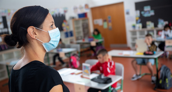 Eine Lehrerin mit Mund- und Nasenschutz steht in einer Grundschule.