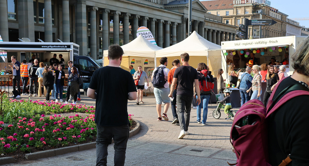 Menschen laufen um ein rundes Blumenbeet, im Hintergrund Info- und Essensstände.