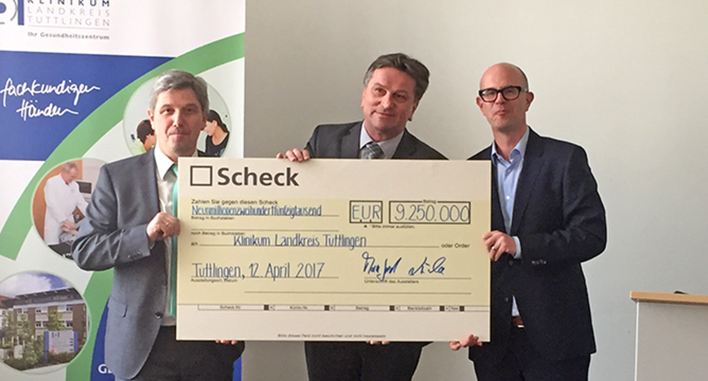 Landrat Stefan Bär, Minister Manne Lucha und Klinikum-Geschäftsführer Sascha Sartor halten gemeinsam einen symbolischen Scheck über 9,25 Millionen Euro.
