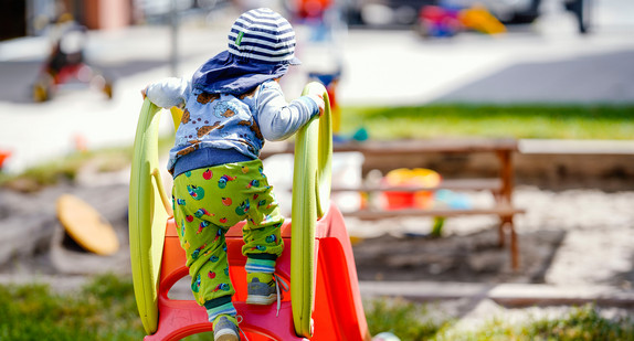 Ein Kind klettert in einer Kindertagesstätte vor einem Sandkasten auf eine Rutsche.