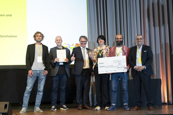 Preisverleihung Integrationspreis des Landes Baden-Württemberg Gruppenfoto der Preisträger von Platz 3 der Kategorie „Unternehmen und Verbände“ mit Minister Manne Lucha auf Bühne.