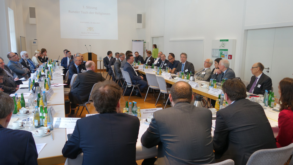 Minister Manne Lucha und die Teilnehmenden des Runden Tischs der Religionen sitzen am 24. Mai 2017 in Stuttgart an einem Konferenztisch