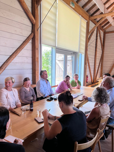 Minister Lucha sitzt mit mehreren Mitarbeitenden des Hofguts Hopfengarten an einem großen Tisch in einer umgebauten Scheune.