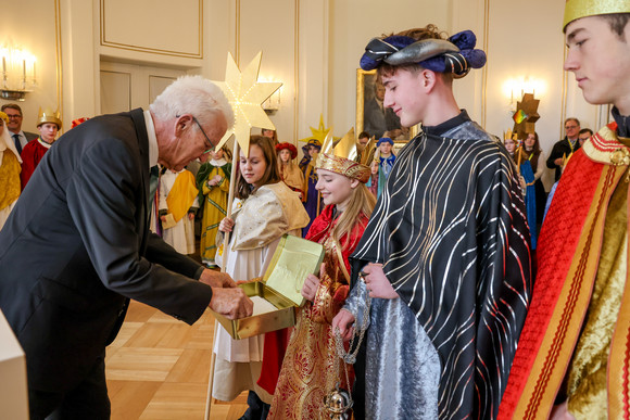 Ministerpräsident Winfried Kretschmann (links) überreicht den Sternsingerinnen und Sternsingern eine Geldspende. 