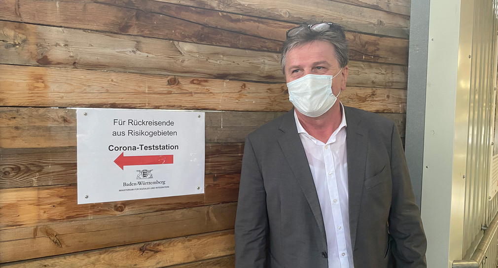 Gesundheitsminister Manne Lucha vor einem Hinweisschild zur Coronavirus-Teststation am Stuttgarter Hauptbahnhof