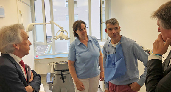 Minister Manne Lucha und AOK-BW-Vorstandsvorsitzender Dr. Christopher Hermann sprechen in der Zahnarztpraxis Dr. Elsäßer in Kernen mit einem Patienten.