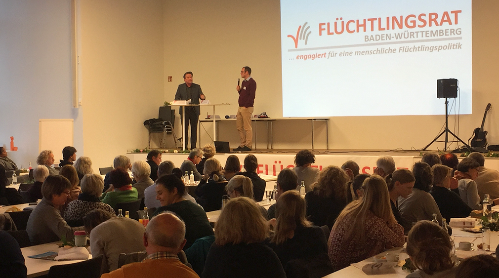 Minister Lucha im Gespräch mit Seán McGinley, Geschäftsführer des Flüchtlingsrates Baden-Württemberg auf einer Bühne