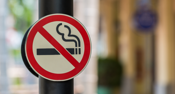 An einer Eingangstür hängt ein Schild, auf dem eine durchgestrichene Zigarette abgebildet ist. In diesem Gebäude herrscht also Rauchverbot.