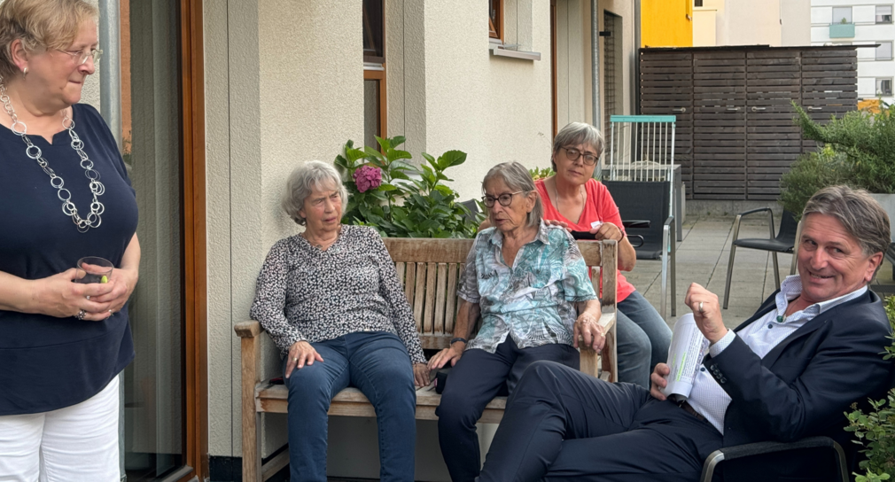 Minister Manne Lucha sitzt mit Bewohnerinnen der Pflege-WG auf der schattigen Terrasse.