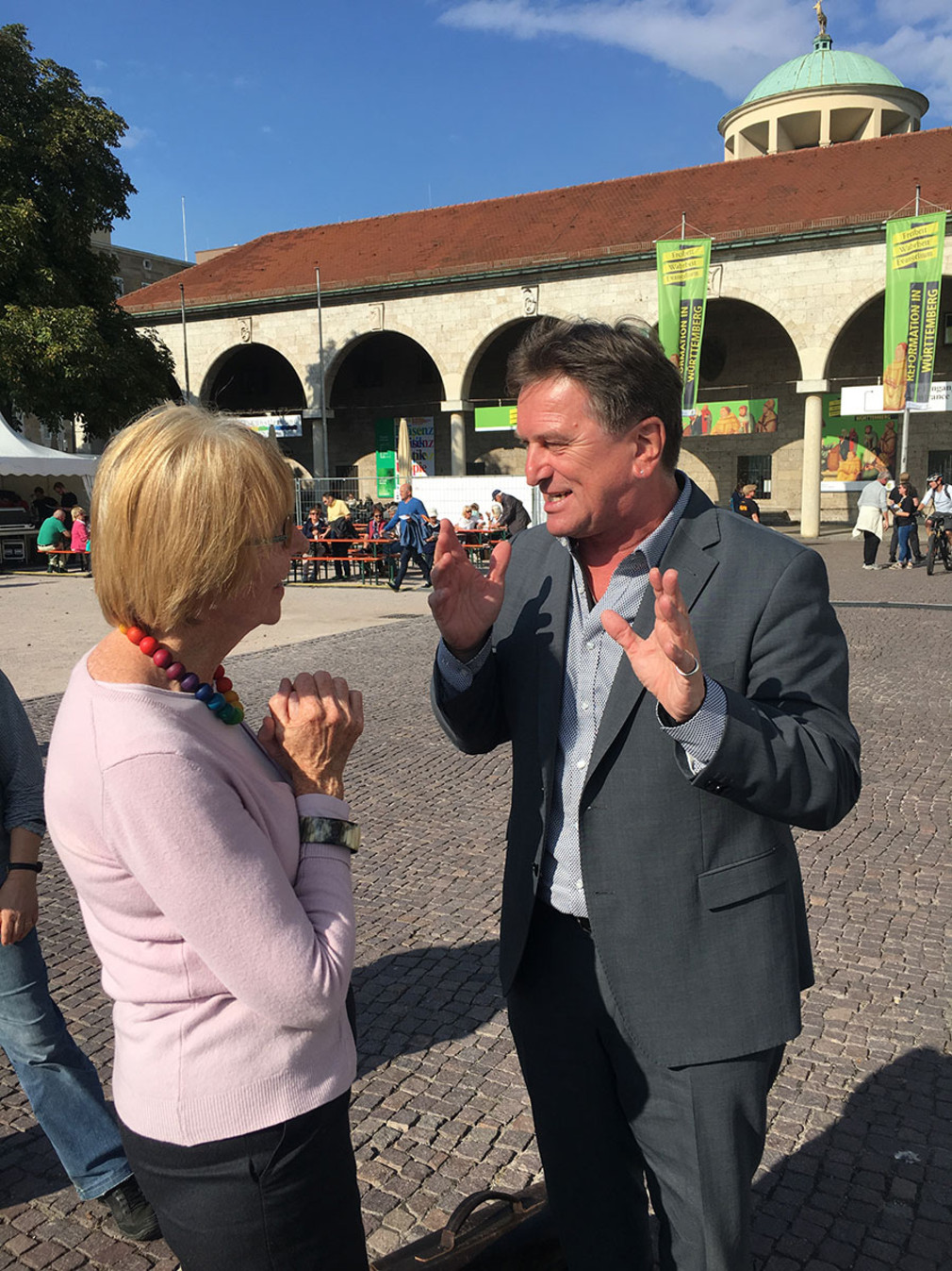 Minister Manne Lucha im Gespräch mit einer Frau auf dem Stuttgarter Schlossplatz