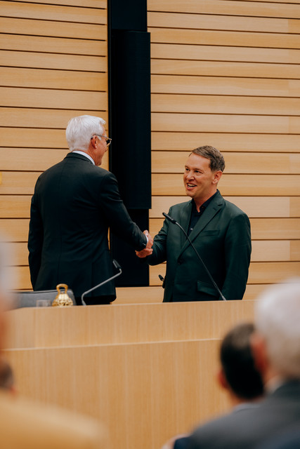 Landtagspräsident Thomas Strobl und Minister Oliver Hildenbrand schütteln sich die Hände auf der Tribüne des Landtags Baden-Württemberg.