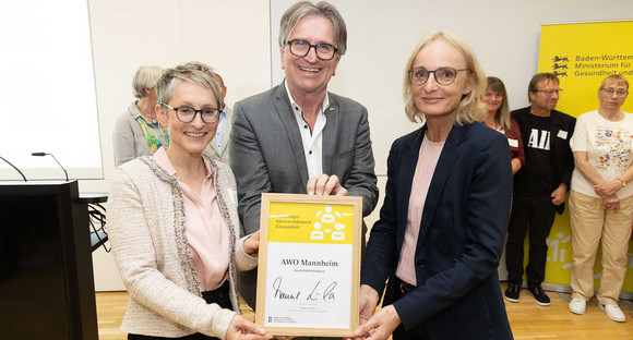 Sozialminister Manne Lucha posiert gemeinsam mit Preisträgern und ihrer Siegerurkunde.