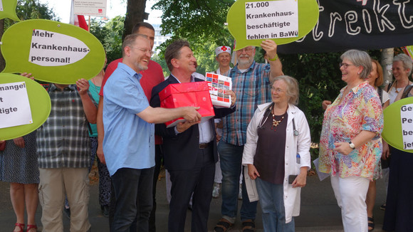 Gesundheitsminister Manne Lucha hält Kiste mit gesammelten Unterschriften für mehr Krankenhauspersonal und spricht mit Demonstranten