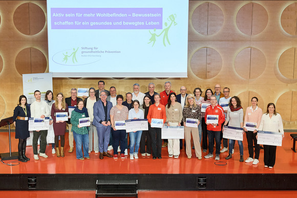 Gruppenfoto: Gesundheitsminister Manne Lucha mit allen Preisträgern des Präventionspreises 2026 auf der Bühne im Hospitalhof Stuttgart.