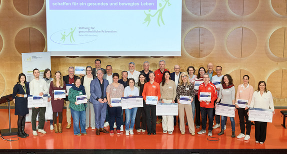 Gruppenfoto: Gesundheitsminister Manne Lucha mit allen Preisträgern des Präventionspreises 2026 auf der Bühne im Hospitalhof Stuttgart.