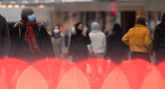 Eine Frau geht mit Mund-Nasen-Schutz hinter roten Lichtern einer Absperrung durch die Innenstadt.