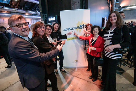 Gruppe von Menschen zeigt auf Roll-up mit dem Hashtag „gemeinsamBW“