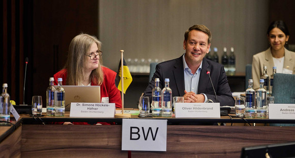 Dr. Simone Höckele-Häfner, Leiterin der Abteilung „Gesellschaft“ im Sozialministerium Baden-Württemberg, sitzt neben Sozialminister Oliver Hildenbrand am Konferenztisch der JFMK 2026 in Hessen.