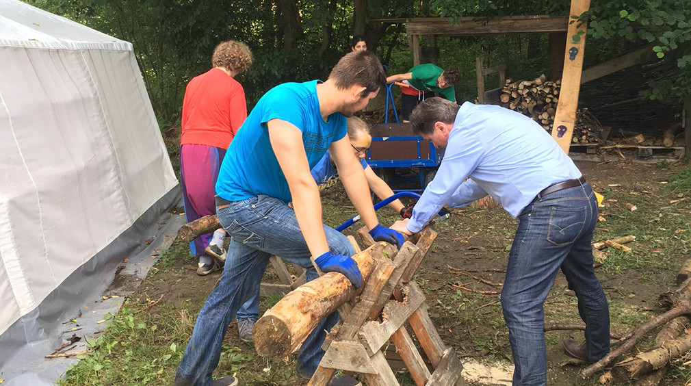 Sozial- und Integrationsminister Manne Lucha hilft jungem Mann beim Holzsägen
