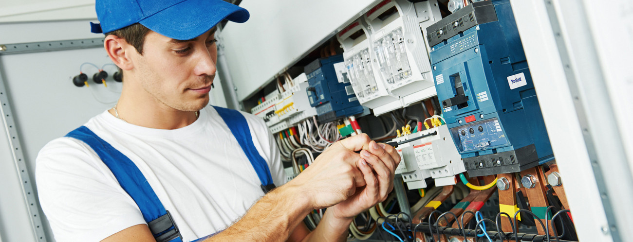 Junger Elektroniker mit Schraubenzieher vor Stromkasten