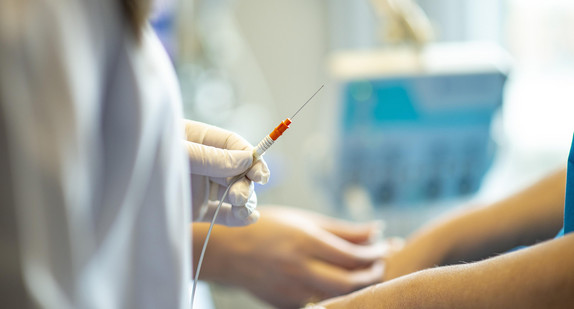 Krankenhauspflegerin hält Katheter in der Hand, im Hintergrund medizinisches Gerät zu sehen.