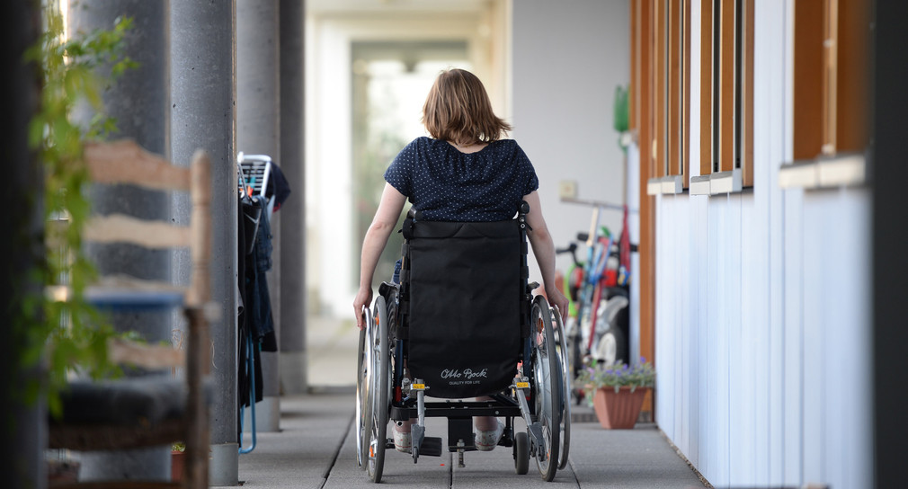 Eine Rollstuhlfahrerin fährt in einer Wohnanlage zu ihrer Wohnung.