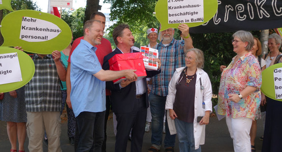 Gesundheitsminister Manne Lucha hält Kiste mit gesammelten Unterschriften für mehr Krankenhauspersonal und spricht mit Demonstranten