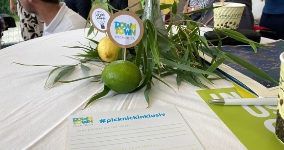 Mit Zitrusfrüchten geschmückter Stehtisch, auf dem ein Formular mit dem Aufdruck #picknickinklusiv liegt. In einer Limette steckt ein Holzstäbchen mit einem runden Schild „DownTown Hechingen“.