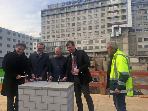 Gesundheitsminister Manne Lucha, Reinhard Schimandl (Geschäftsführer Klinikum Stuttgart), Fritz Kuhn (Oberbürgermeister Landeshauptstadt Stuttgart) und Dr. Markus Koch (Vorstandsvorsitzender BAM Deutschland) stehen auf Baustelle um Grundstein herum