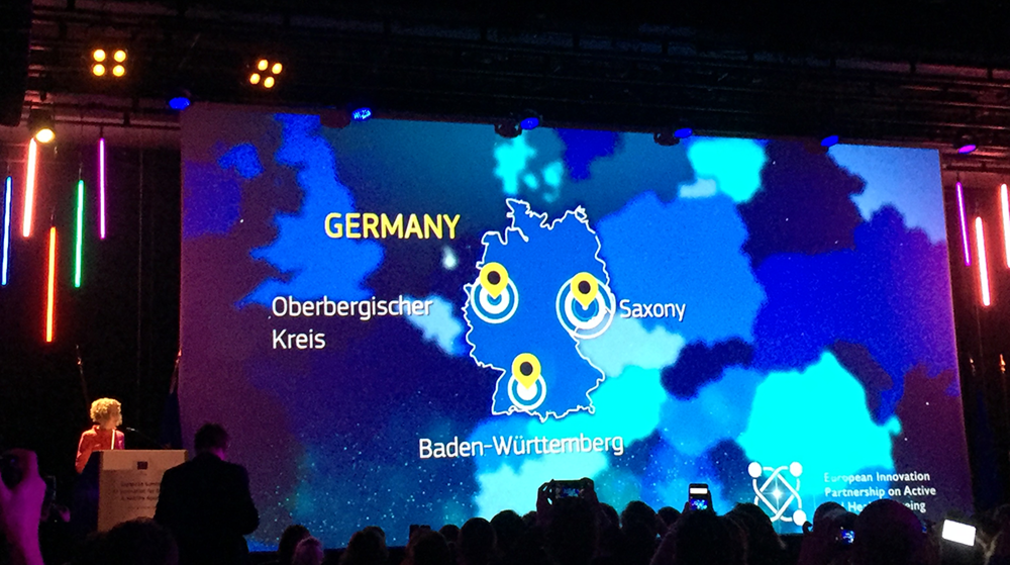 Präsentation auf Bühne zeigt Karte von Deutschland mit drei markierten Punkten: Baden-Württemberg, Sachsen und Oberbergischer Kreis
