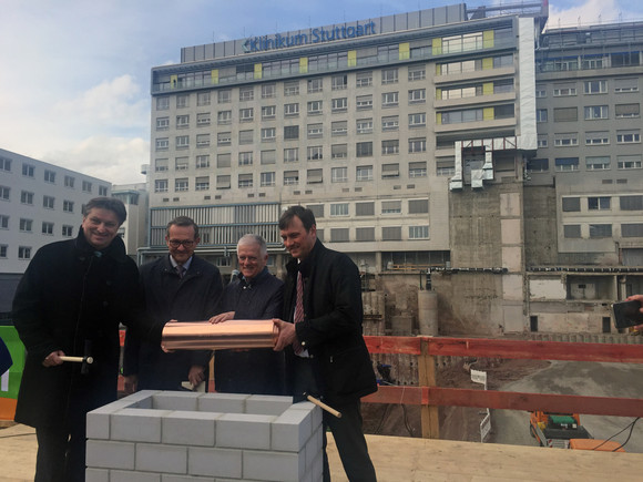 Gesundheitsminister Manne Lucha, Reinhard Schimandl (Geschäftsführer Klinikum Stuttgart), Fritz Kuhn (Oberbürgermeister Landeshauptstadt Stuttgart) und Dr. Markus Koch (Vorstandsvorsitzender BAM Deutschland) stehen auf Baustelle um Grundstein herum