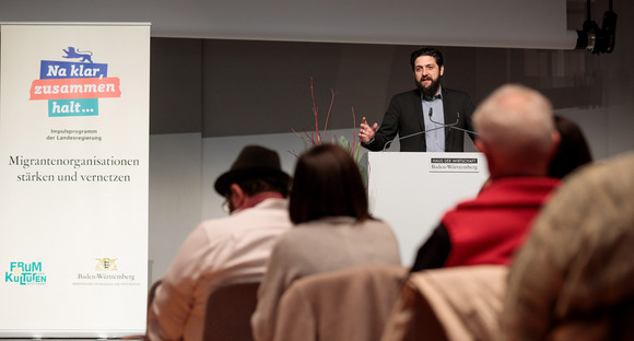 Integration Erster Landesfachtag Migrantenorganisationen in Stuttgart Professor Aladin El-Mafaalani steht an Redepult vor Publikum