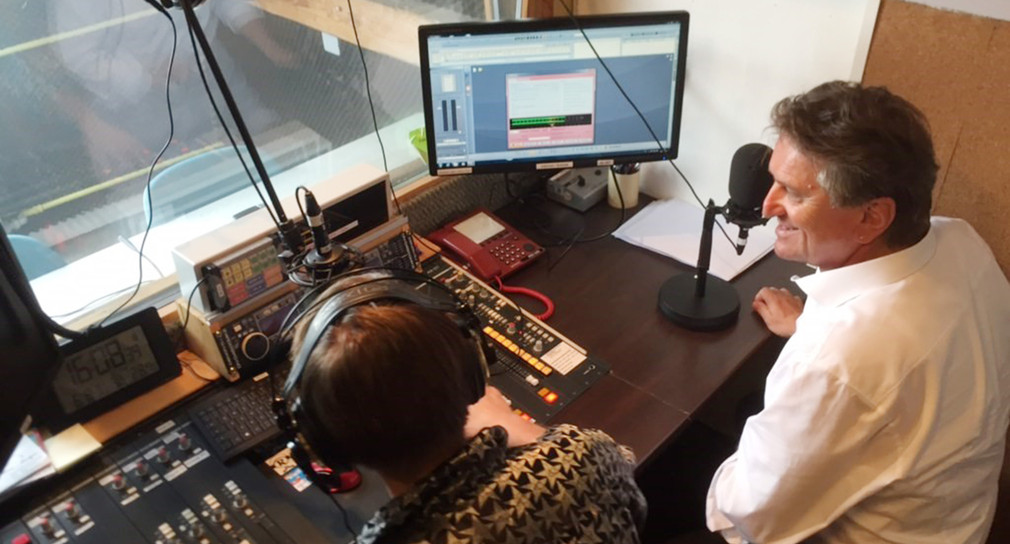 Minister Manne Lucha sitzt vor einem Mikrofon in einem Aufnahmestudio des Freien Radio Freudenstadt