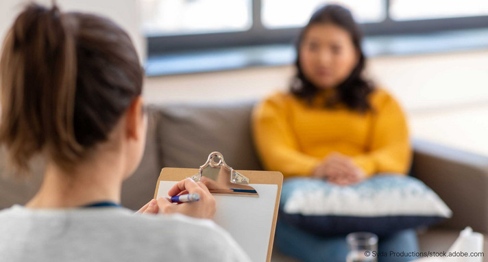 Frau mit Notizklemmbrett sitzt Frau auf Sofa gegenüber.