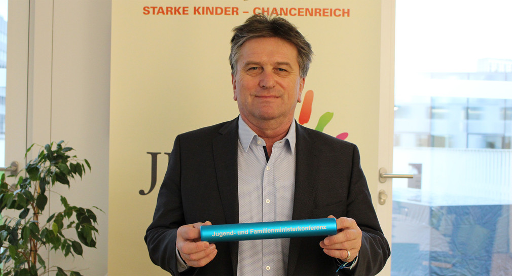 Sozial- und Integrationsminister Manne Lucha hält Stab mit Aufschrift "Jugend- und Familieministerkonferenz". (Bild: Sozialministerium Baden-Württemberg)