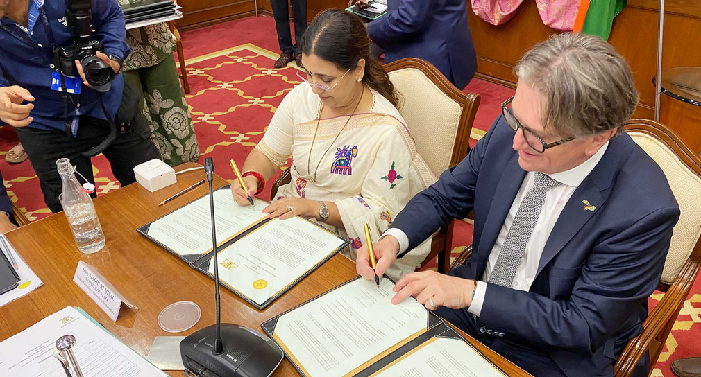 Minister Manne Lucha und Staatsministerin Madhuri Misal des indischen Bundesstaats Maharashtra sitzen nebeneinander an einem Tisch und unterzeichnen Dokumente.