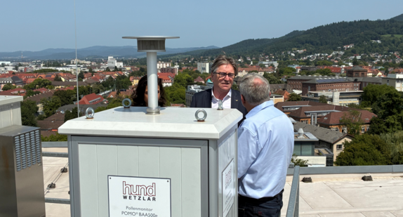 Minister Manne Lucha lässt sich von einem Mitarbeiter des Deutschen Wetterdienstes die Funktion eines Pollenmonitors erklären. Das Gerät steht auf dem Dach des Zentrums für Medizin-Meteorologische Forschung in Freiburg. Im Hintergrund sieht man das tolle Panorama der Stadt im Breisgau.