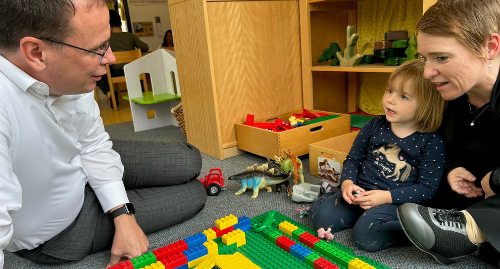 Staatssekretär Volker Schebesta und Landes-Behindertenbeauftragte Simone Fischer spielen Lego mit Kita-Kind.